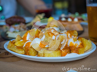 Closeup of Spanish fried potato cubes with sauce in a plate on the table under the lights Stock Photo