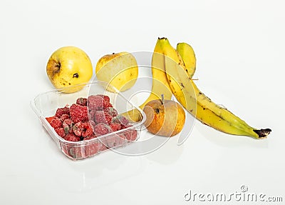 Closeup of spoilt raspberries in a plastic container, a banana peel and apples on a white background Stock Photo