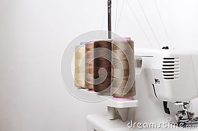 Closeup of spool of beige threads and professional overlock macnine against white background Stock Photo