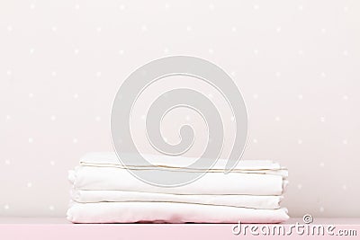 Closeup of a stack of clean white bedding on a table by a light wall. Copy space Stock Photo