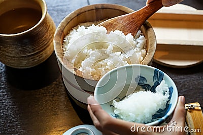 Closeup steamed japanese white rice in traditional wooden bowl with serving hands and wooden table background Stock Photo
