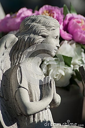 stoned angel praying at cemetery with purple flowers Stock Photo