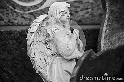 stoned angel praying on tomb at cemetery Stock Photo