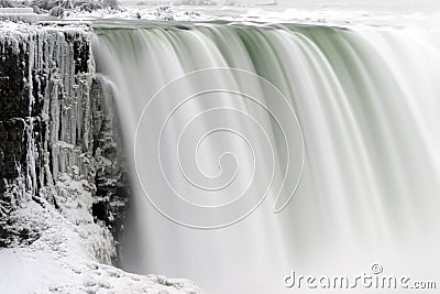 Closeup of strong waterfall flowing over ice covered cliff, smooth waters Stock Photo