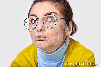 Closeup studio portrait of doubtful young woman with a bun hairstyle, wearing casual outfit and round transparent eyewear, looking Stock Photo