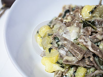 Closeup of succulent and typical Italian dish Pizzoccheri in a white plate on a table. Typical dish from Valtellina, Lombardy, Stock Photo