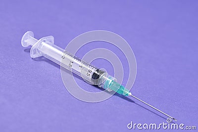 Closeup of a syringe needle with the vaccine against a purple background - COVID-19 Stock Photo