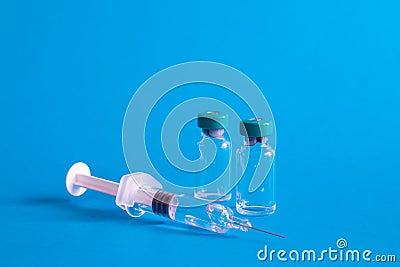 Closeup of a syringe needle with the vaccine ampoules against a blue background - COVID-1 Stock Photo