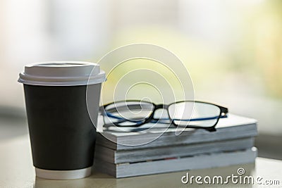 Closeup of takeaway papercup of hot coffee with stack of books and reading glasses on wooden table Stock Photo