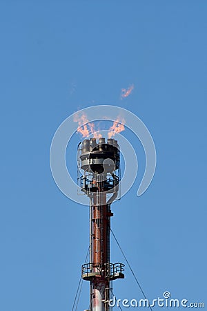 Oil Refinery Equipment with Orange Flames, against Pure Blue Sky Stock Photo