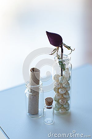 Closeup of three small glass jars with vintage pearls, old parchment and dry rose bud on bright window background Stock Photo