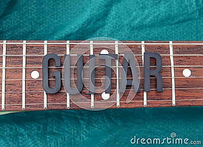 Closeup to a GUITAR lettering black word over a six electric guitar strings and wooden fretboard over a green background Stock Photo