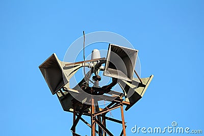 Closeup of top of tall strong metal structure holding four large public civil defence warning air sirens Stock Photo