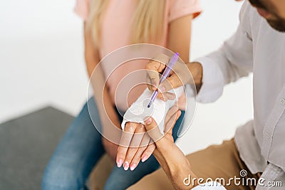 Closeup top view of unrecognizable male friend writing inscription on cast of woman with broken hand wrapped in plaster Stock Photo