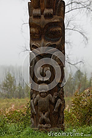 Closeup of traditional carved Gitxsan totem poles with mist covered forest behind Stock Photo