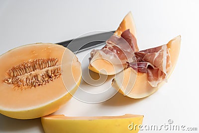Closeup of two melon slices with cured ham slices on top, surrounded by half melon and a knife Stock Photo