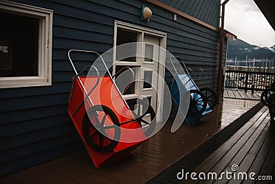 Closeup of two wheelbarrows leaning on a wooden building wall during the rain Stock Photo