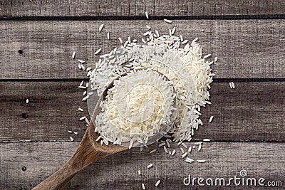 Closeup uncooked dry Thai jasmine rice are overflow in wooden ladle on wooden floor, flat lay and top down horizontal view. Stock Photo