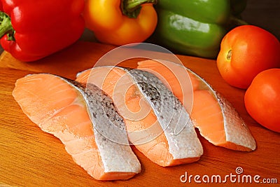Closeup uncooked sliced salmons on a cutting board surrounded with colorful fresh vegetables Stock Photo