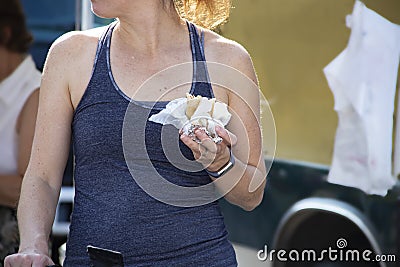 Closeup of unrecognizable girl in sleveless teeshirt with exercise wristband eating food from food truck outdoors Stock Photo