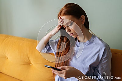 Closeup of upset unhappy young woman lady with redhaired in comfy homewear sitting on couch, using phone at home Stock Photo