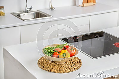 Closeup of vegetables in the bowl in modern white kitchen with induction cooking heater and sink on background Stock Photo