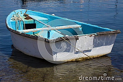 Closeup View of Dinghy Paddle Boat on Clear Water. Oar, rusty Chain and Rope Resting inside the Blue Watercraft. Vessel Stock Photo