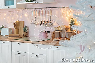 Closeup view on interior of modern white kitchen with pink walls and blue decor on a Christmas New year eve. Pine tree with lights Stock Photo