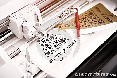 closeup view on machine head of plotting machine that cuts christmas sticker with lettering from black adhesive vinyl. Stock Photo