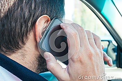 Closeup view of a man holding a mobile phone near his ear and talking on it while driving. Danger of using the phone in a car Stock Photo