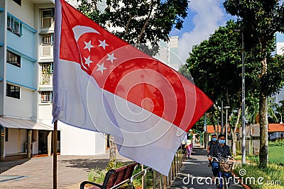 Closeup view of Singapore flag waving in the wind, cyclists riding by, on bright sunny day. HDB neighbourhood in background Editorial Stock Photo