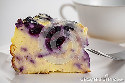 Closeup view slice of yogurt blueberry cake with metal fork in white ceramic dish Stock Photo