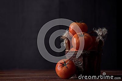 Closeup view of tomatoes with waterdrops on it placed in a wooden bowl on a wooden table Stock Photo