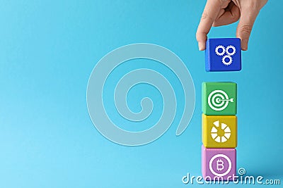 Closeup view of woman stacking colorful cubes with different images on light blue background, space for text. Management concept Stock Photo