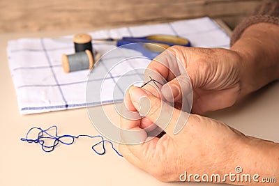 Closeup view of woman threading needle at beige table, space for text Stock Photo