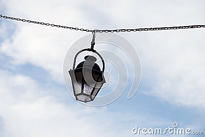 vintage street light suspended on metallic chain in the street on cloudy sky background Stock Photo