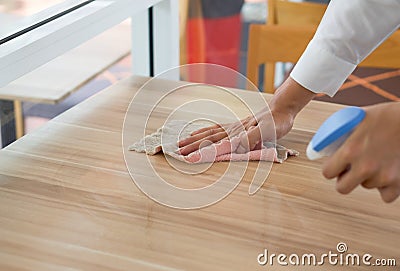 Closeup waiter`s hand use a liquid cleaner and a towel to wipe off the stains on the table Stock Photo