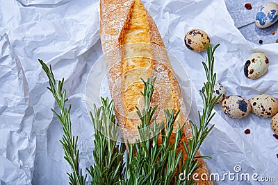 Closeup of wheat baguette, twigs of fragrant rosemary, little quail eggs on a light gray background. Stock Photo