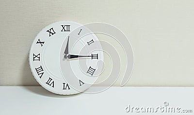 Closeup white clock for decorate show a quarter past twelve or 12:15 a.m. on white wood desk and cream wallpaper textured backgrou Stock Photo