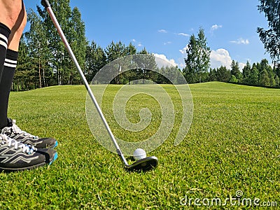 Closeup of white golf ball and club. Human feet on green grass Stock Photo