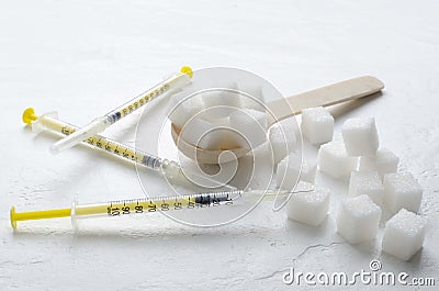 Closeup of white sugar, insulin syringes and wooden spoon ful of sugar cubes on the white surface Stock Photo