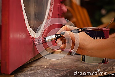 Closeup of woman hand with brush painting carved ornaments on lower part of door of antique cupboard made of wood in Stock Photo