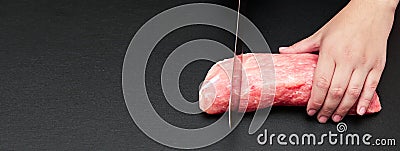 Closeup of the woman hands of a butcher cutting slices of raw meat off a large loin on black background with copy space Stock Photo
