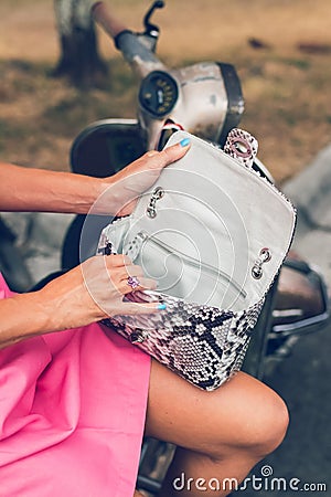 Closeup woman hands with fashion luxury snakeskin python handbag on a retro motorbike background. Outdoors, Bali island. Stock Photo
