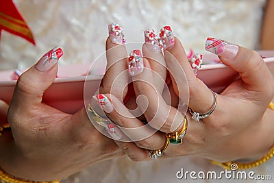 Closeup of a woman`s fingers with beautiful manicure and many rings in white dress and holding pink dish. Stock Photo