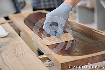Closeup of workers hand covering wooden plank with finishing protective cover for wood Stock Photo