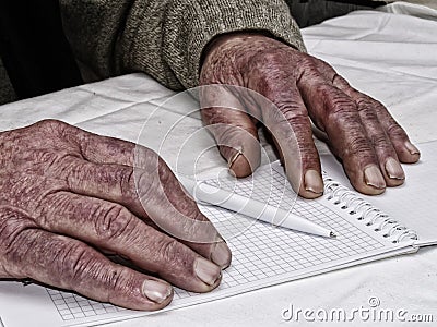 Closeup of the wrinkled hands of man holding pen and paper, wearing a green sweater Stock Photo