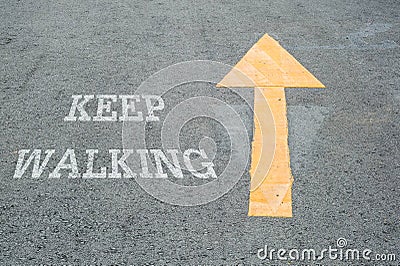 Closeup yellow painted arrow sign on cement street floor with white keep walking word textured background Stock Photo