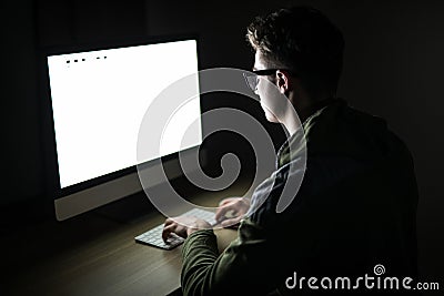 Closeup of young man sitting and using blank screen computer in dark room. hacker or programmer in dark room. Stock Photo