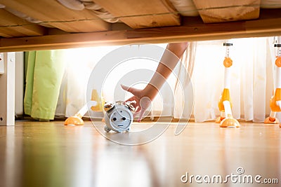 Closeup of young woman reaching under the bed and pressing snooze button on alarm clock Stock Photo